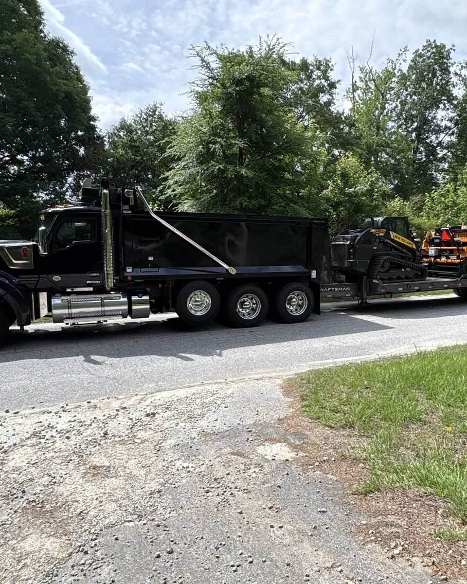 Asphalt Appeal dump truck towing a trailer loaded with the paver and skid steer